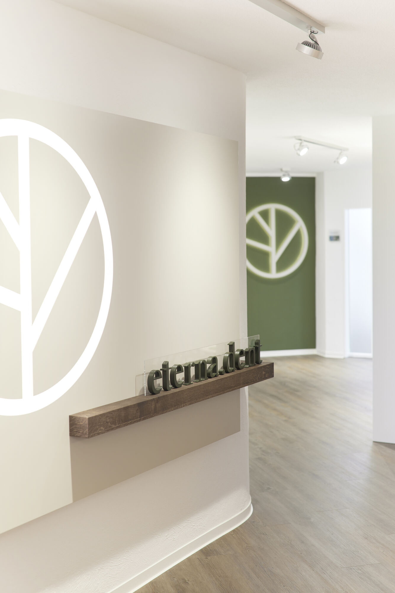 r_06A0074 Heller Flur der Zahnarztpraxis mit großem runden Logo an der Wand und modernem Design, der in die Behandlungsräume führt