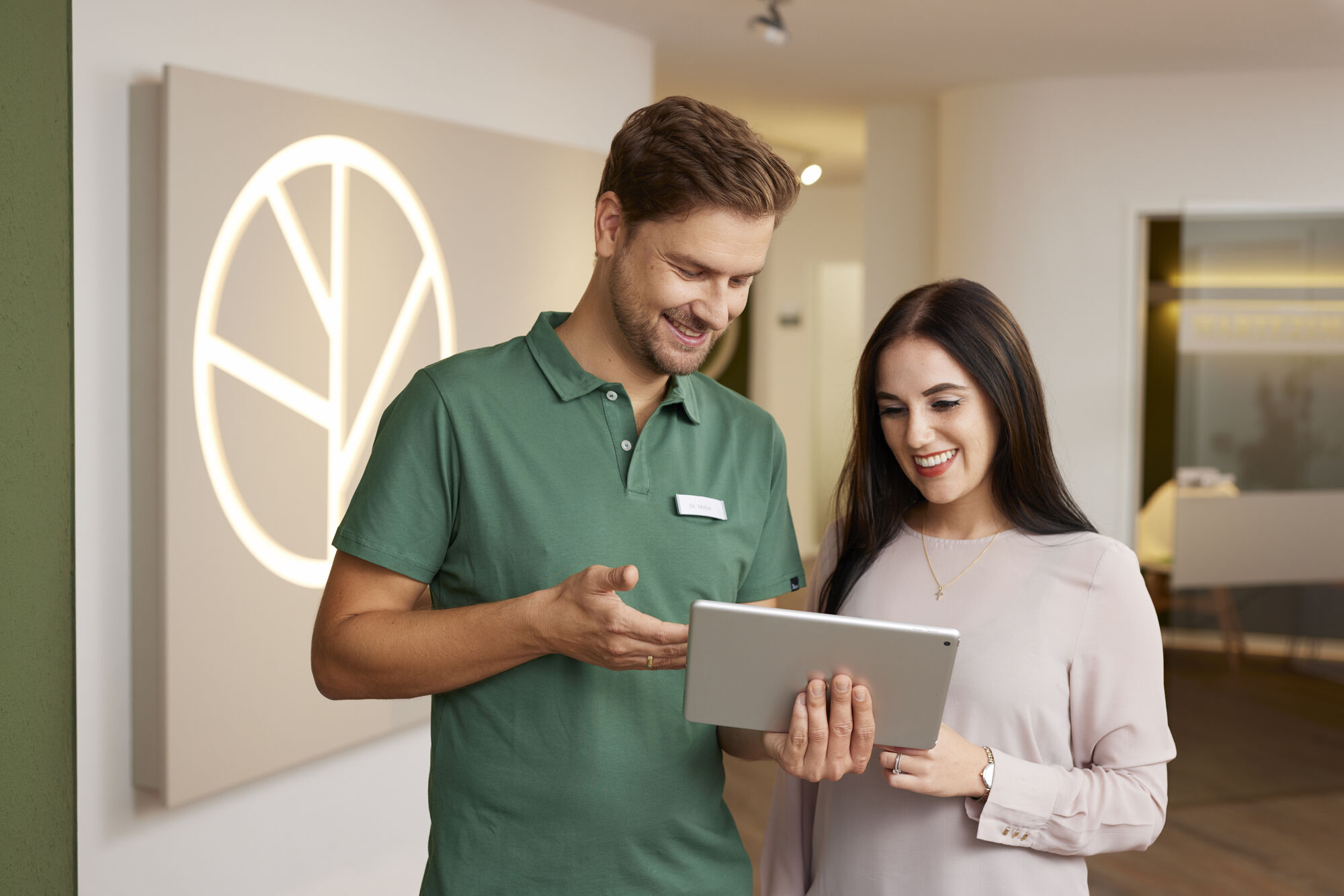 r_06A0164 Dr. Möller erklärt einer Patientin freundlich Behandlungsdetails auf dem Tablet im hellen Eingangsbereich der Zahnarztpraxis