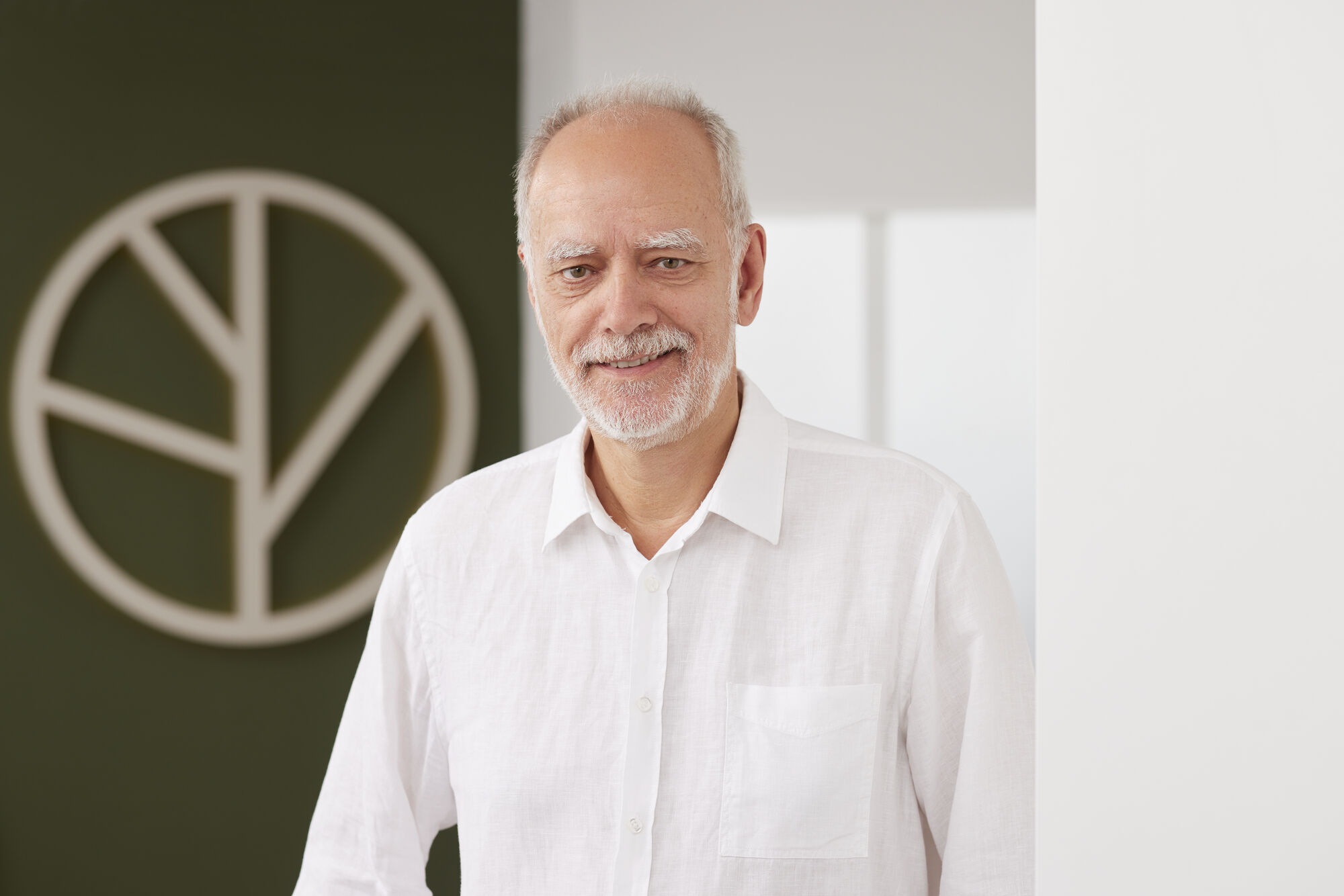 Dr. Joachim Beck steht im weißen Hemd vor heller Wand, lächelt freundlich in die Kamera, wirkt offen und nahbar im Porträtstil aufgenommen